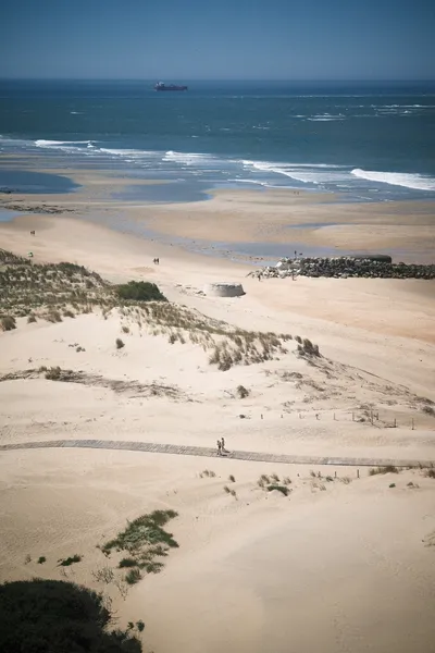 Two people walking down a wooden path on the beach, the view stretches over the ocean to the horizon