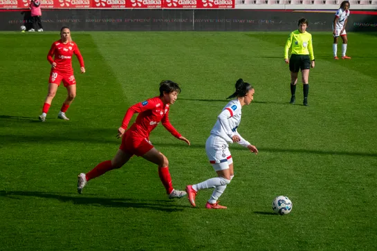 One football player chases another, their eyes focused on the ball. Teammates and the referree look on
