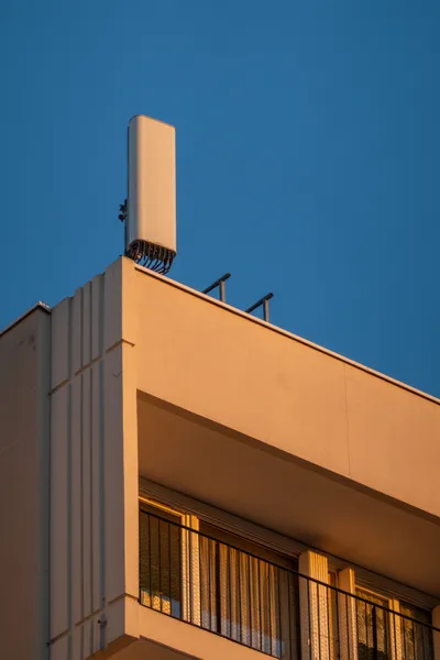 A tenement building flat rooftop, a small 4G radio tower above, both lit orange by the sunset