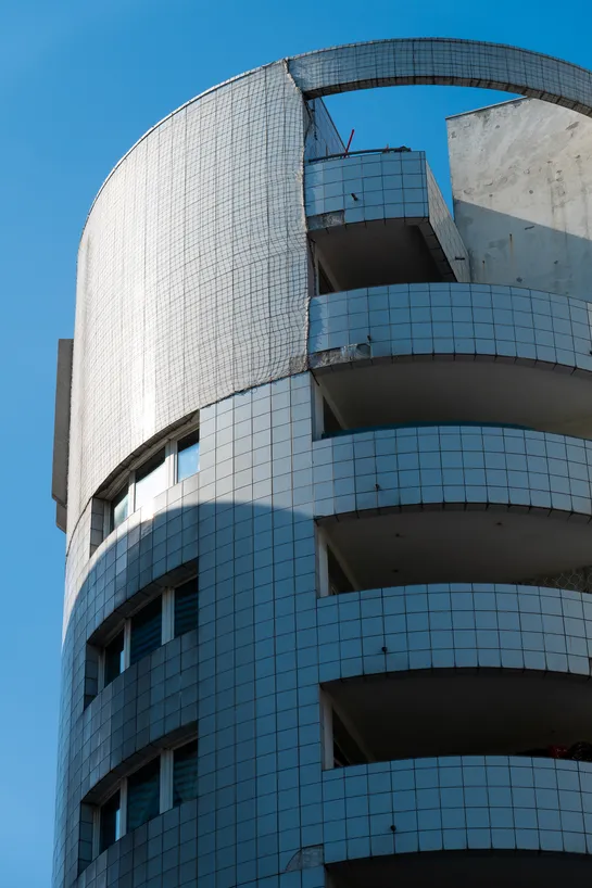 A modern looking building, covered with ceramic tiles. It looks unmaintained, with a net above to prevent more tiles from falling.