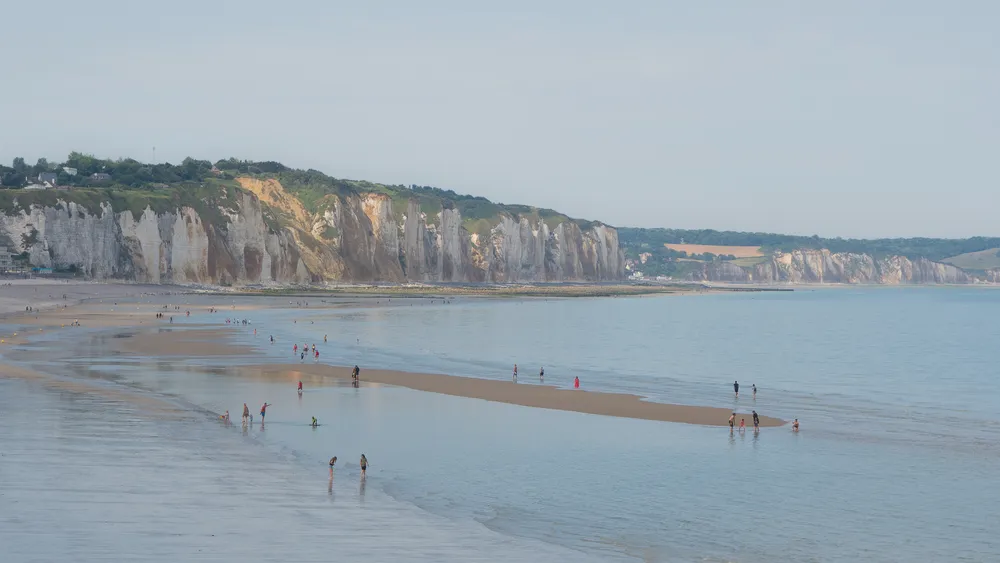 The coast, in the foreground is the beach, hundreds of people can be seen yet they're all far apart from each other. In the background are great cliffs, white and orange.