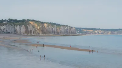 The coast, in the foreground is the beach, hundreds of people can be seen yet they're all far apart from each other. In the background are great cliffs, white and orange.