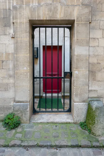 In a stone building, a wrought iron door protects a red door