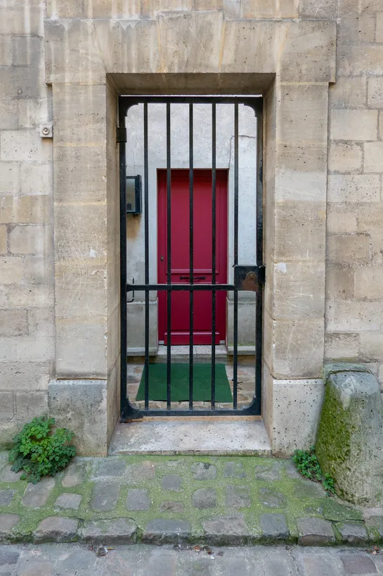 In a stone building, a wrought iron door protects a red door