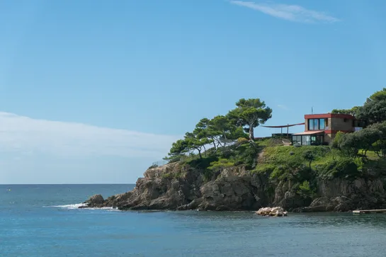 Coastal area with a small cliff, a modern looking house on top, with a few trees