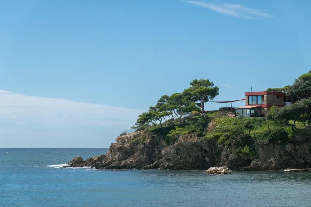 Coastal area with a small cliff, a modern looking house on top, with a few trees