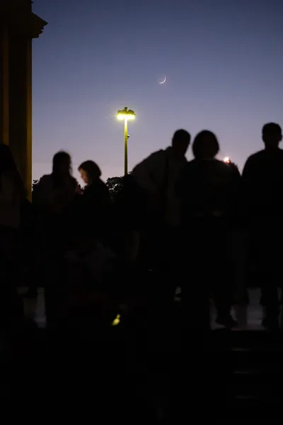 Sihouettes of people in the night, the last light in the sky, a very thin crescent of the moon