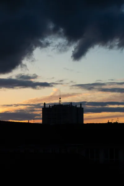 Sunset, dark clouds above, a dark building at the bottom center