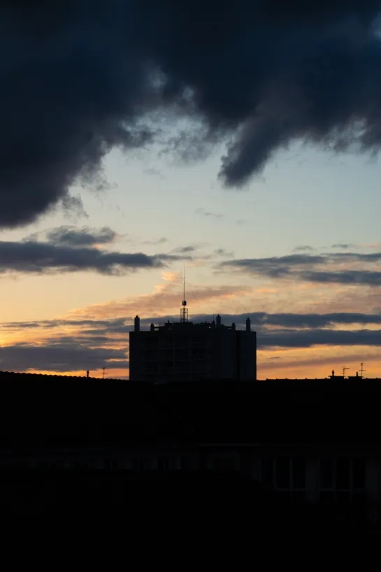 Sunset, dark clouds above, a dark building at the bottom center