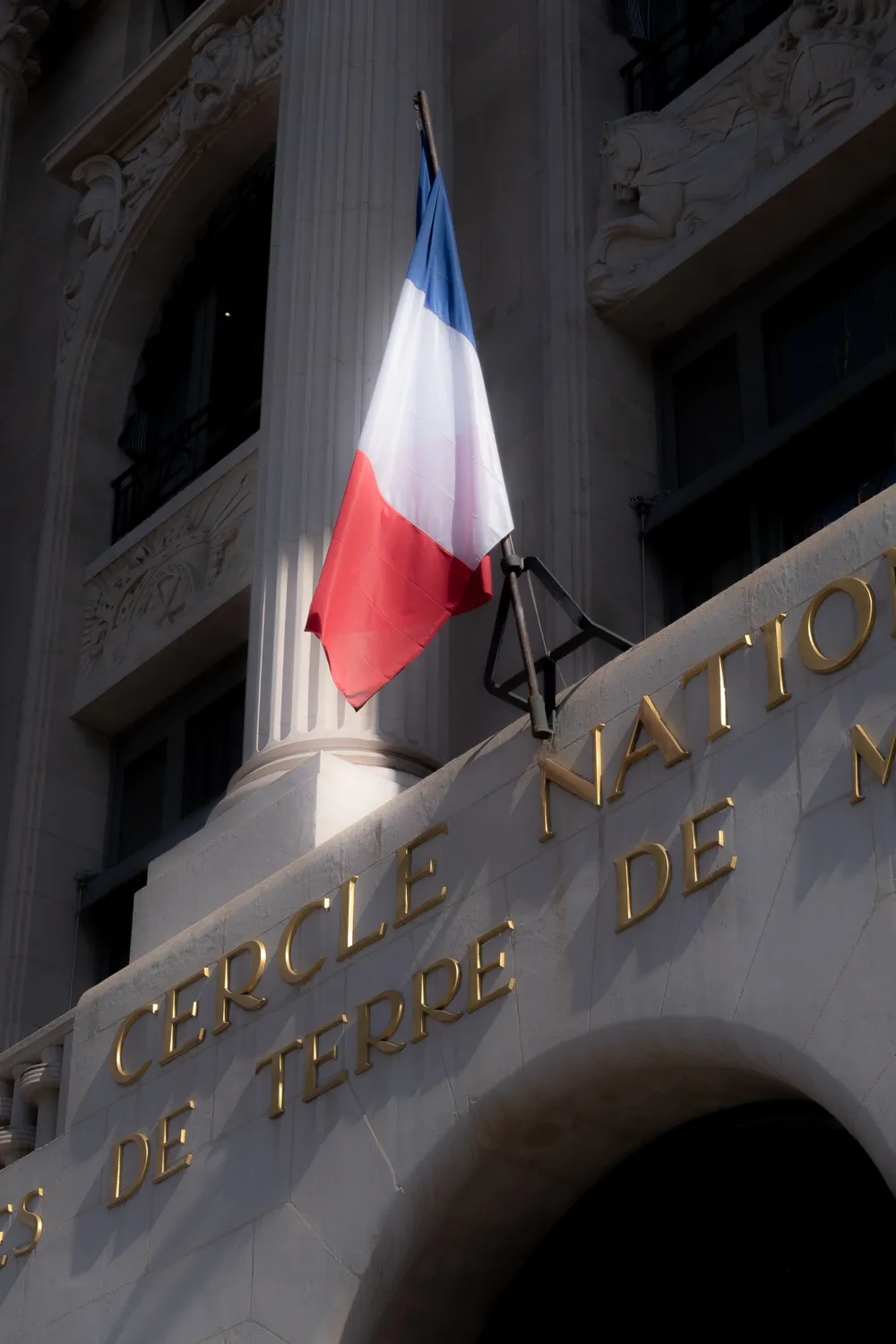 A French flag floats above gilded lettering on a stone building