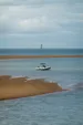 A small boat anchored in a small bay formed by a sand bank, a light house on the horizon