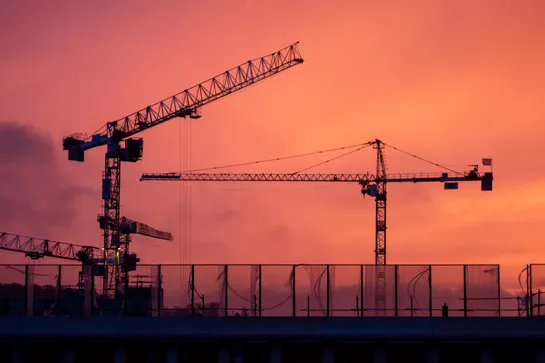 Sunrise, a mix of clouds and fogs leads to a red sky. Two cranes operate in the foreground.