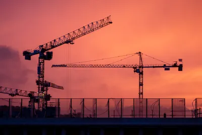 Sunrise, a mix of clouds and fogs leads to a red sky. Two cranes operate in the foreground.
