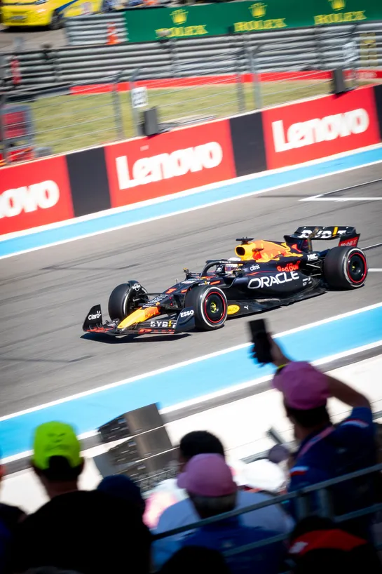 A Red Bull Formula 1 car drives past with fans watching on, some filming with their phone