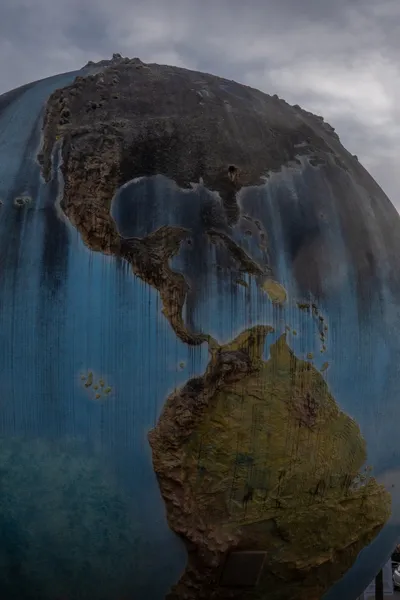 A giant globe representing Earth, grime has covered North America and drips down the Carribean and South America