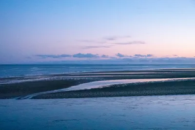 A partially flooded sand bank during sunset, the water reflecting the dim blue sky