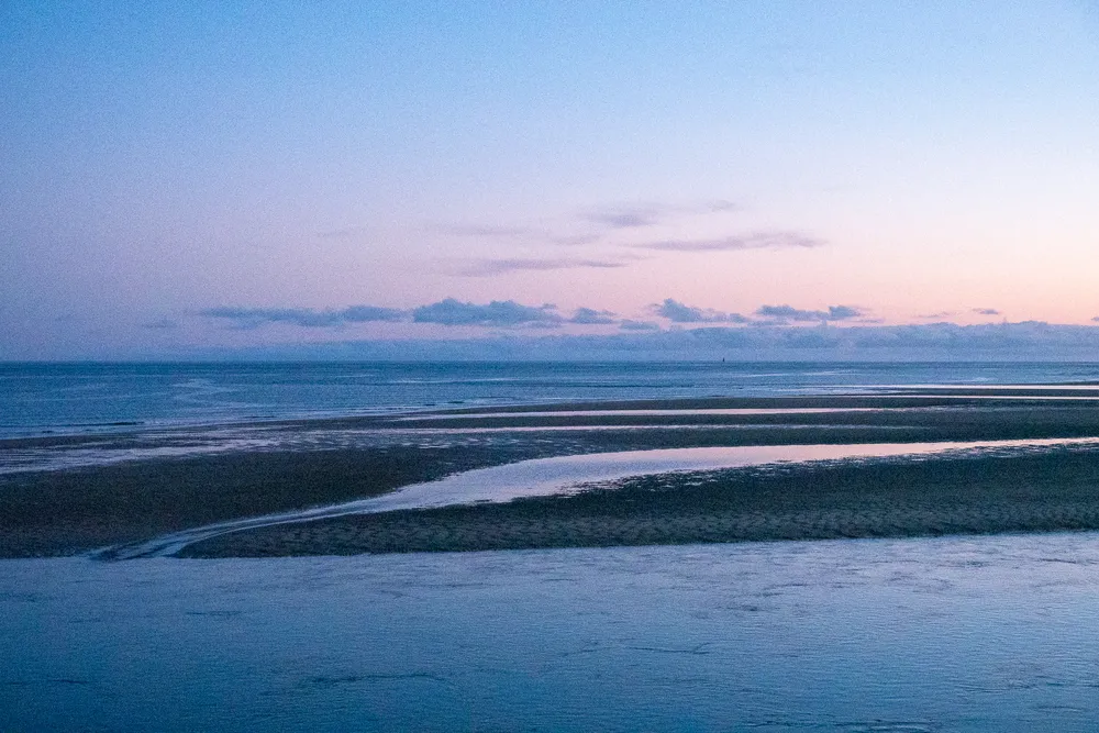 A partially flooded sand bank during sunset, the water reflecting the dim blue sky