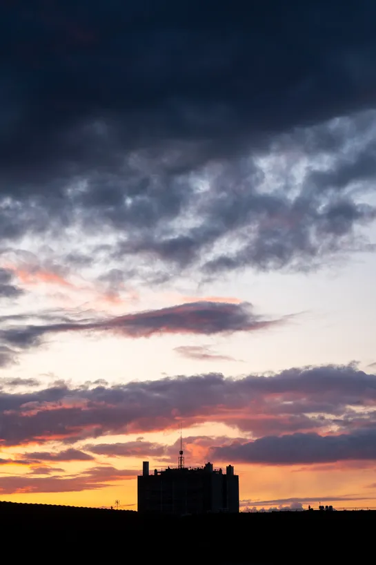 Sunset, dark clouds above, a dark building at the bottom center