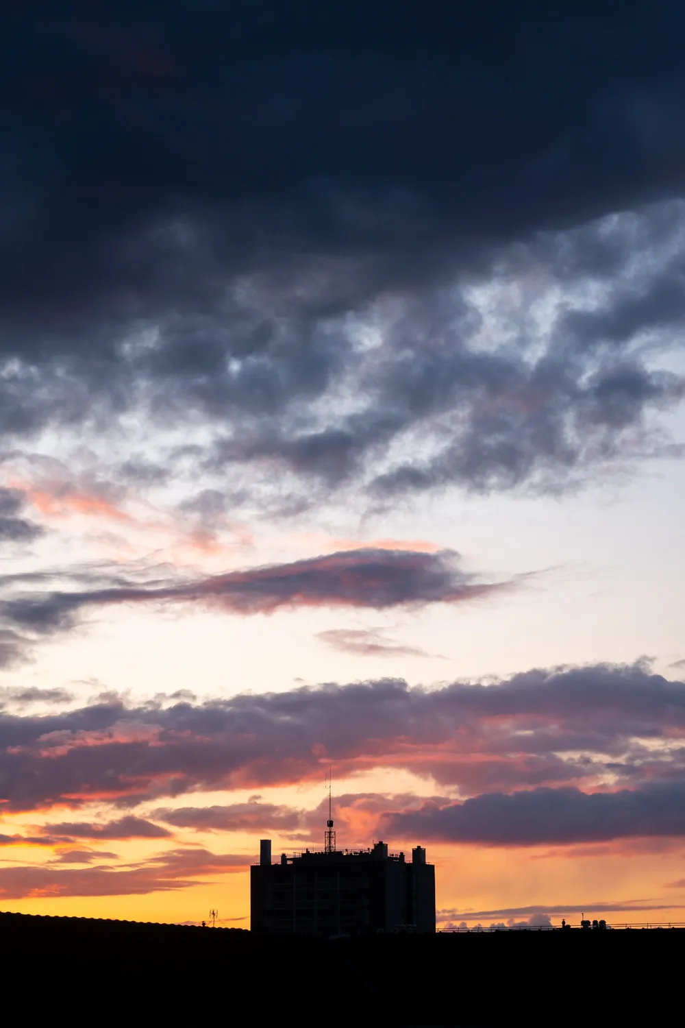 Sunset, dark clouds above, a dark building at the bottom center