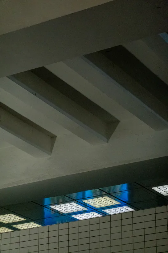 A concrete ceiling, a passage way is lit by bright lights and a blue screen