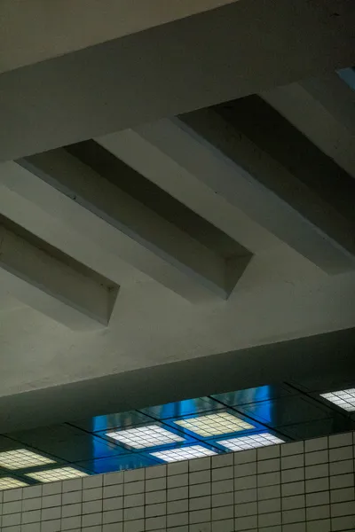 A concrete ceiling, a passage way is lit by bright lights and a blue screen