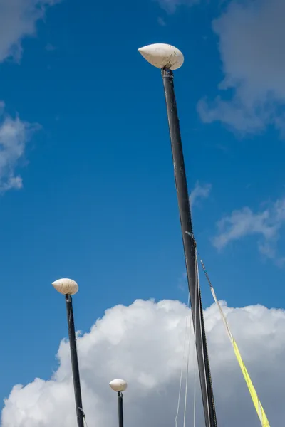 Masts of boats in front of a blue sky with some clouds at the bottom