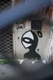 A graffiti of a cartoon figure, with a sideways eye as a head, on a wall in a neglected part of a street