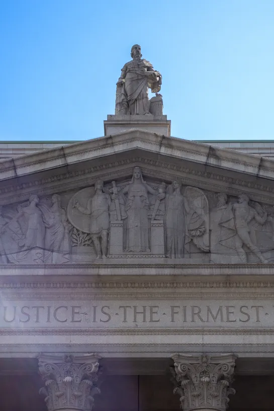 The front of the New York County Supreme Court, a white statue above and gravings below.