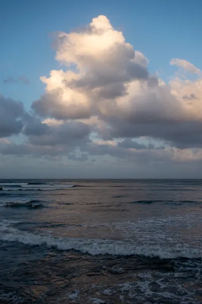 The sea, dimly lit, small waves crashing down. A large cloud reflects the last light of the day, its light in turn reflected by the sea.