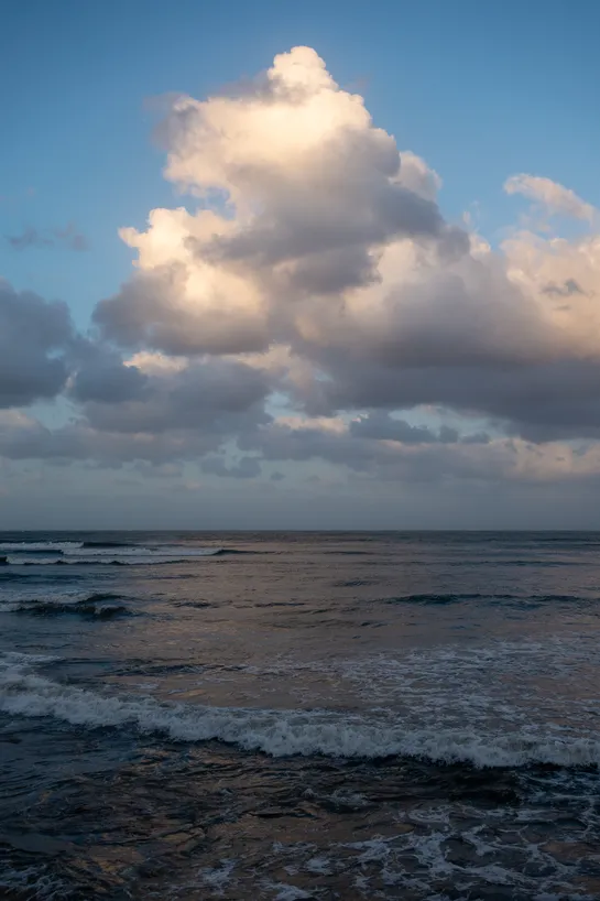 The sea, dimly lit, small waves crashing down. A large cloud reflects the last light of the day, its light in turn reflected by the sea.