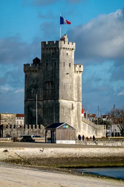 A stone tower partially lit by the sun, a French flag flying above it