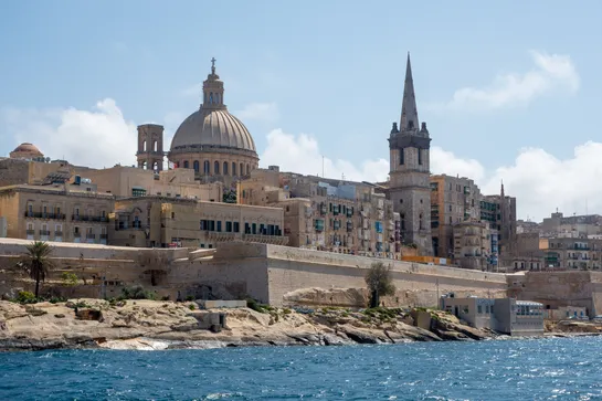 A cathedral and a tower seen above many buildings near the sea