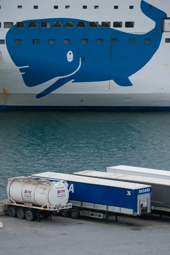 Parked trailers near water, a giant blue whale livery on a ship in the background