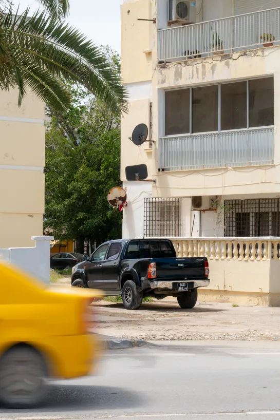 A pickup truck parked next to a residential building as a taxi zooms past