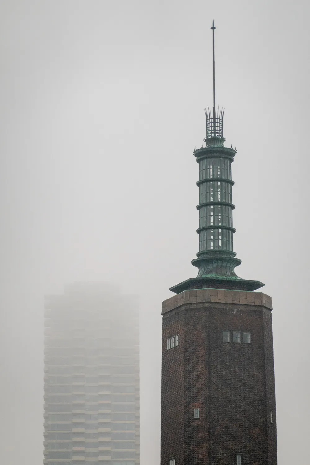 Two tall towers, a residential building on the left is farther and barely visible through the fog