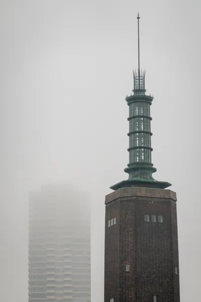 Two tall towers, a residential building on the left is farther and barely visible through the fog