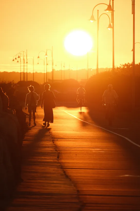 People walking and biking on a path, lit by the setting sun in the distance