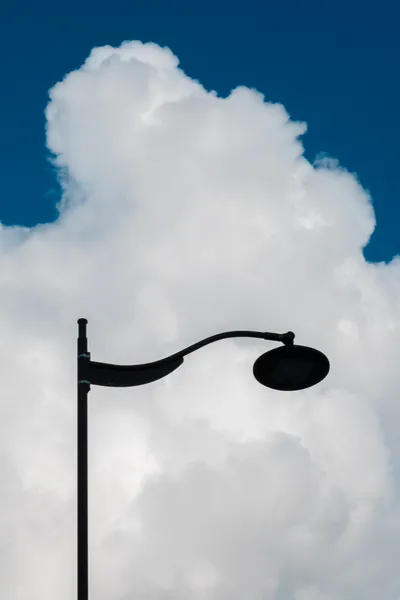 A streetlamp in front of a great white cloud in the blue sky