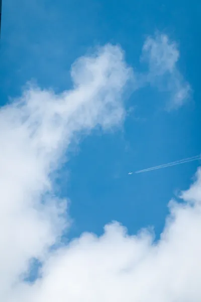 A plane far above, visible in a hole in white clouds