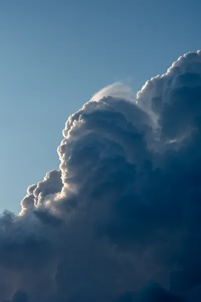 A big cloud forming, the sun lighting its left side, the bottom right is much darker