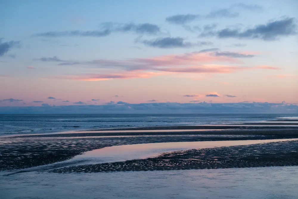 A partially flooded sand bank during sunset, the water reflecting the dim blue sky