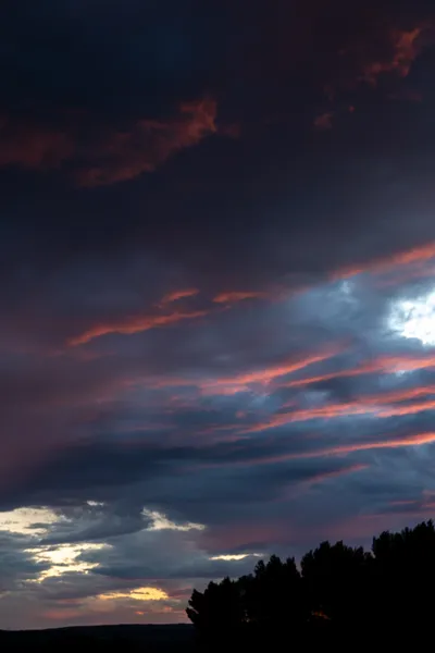 A dramatic cloudy sky, with the sunset lighting part of it pink, the rest remaining deep purple