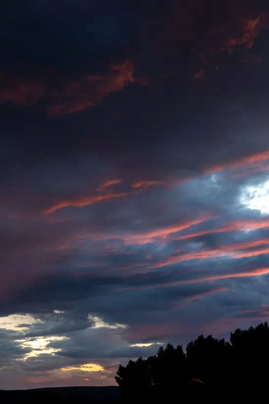 A dramatic cloudy sky, with the sunset lighting part of it pink, the rest remaining deep purple