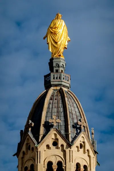 A gilded statue stands above a classically constructed tower