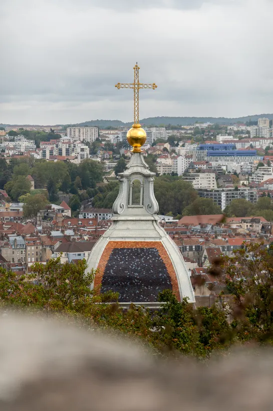 A church rooftop with its large gilded cross, with the rest of the city rooftops in the background
