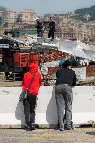 Two people looking on as a ferry ramp comes down with two operators on it, city buildings in the background