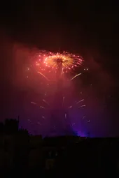 Fireworks fired from the top of the Eiffel Tower, the smoke is forming a gradient : red at the top, purple at the base