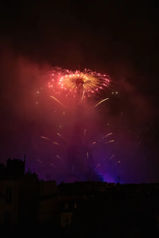 Fireworks fired from the top of the Eiffel Tower, the smoke is forming a gradient : red at the top, purple at the base