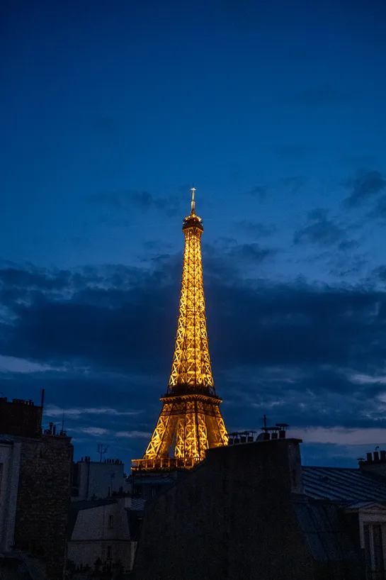 The Eiffel Tower, lit in gold yellow, among the dark blue sky past sunset