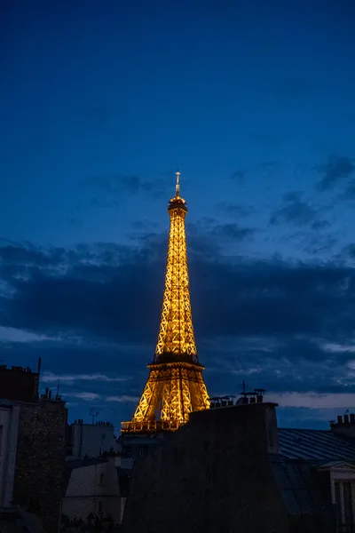The Eiffel Tower, lit in gold yellow, among the dark blue sky past sunset